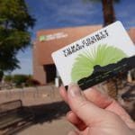 Photo of a hand holidng a library card in front of the Main Yuma County Library.